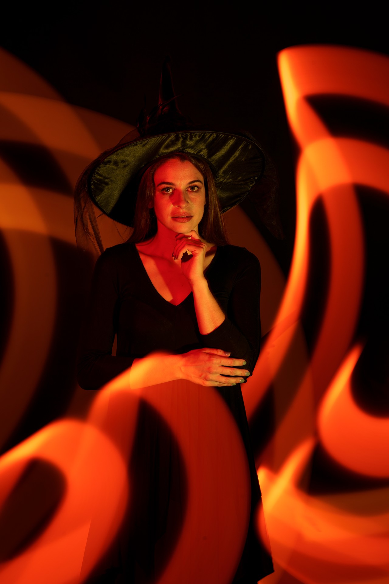 Model in witch hat surrounding by swirls of orange light
