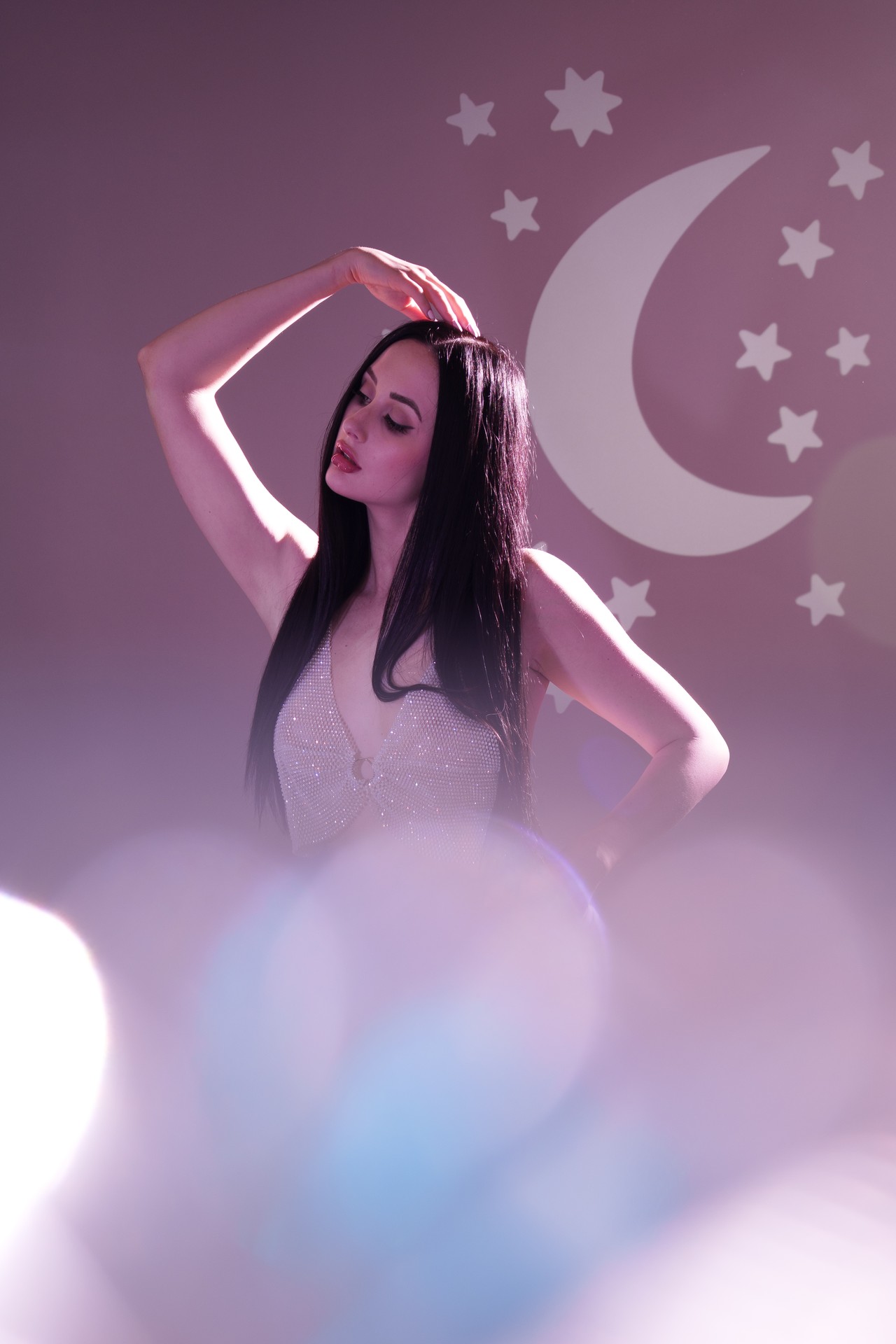 Woman in sparkly top with cartoon moon behind her and sparkly blocking foreground